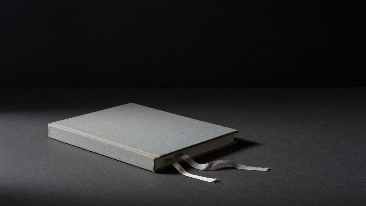 A grey cloth-bound casebook lying closed on a dark surface, two ribbon markers trailing from it.