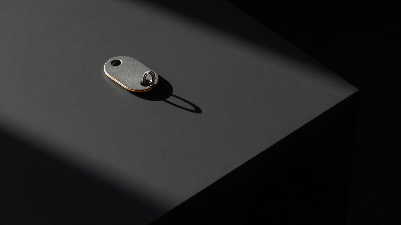 A small steel hardware token lying alone on a dark surface, its keyring loop empty.
