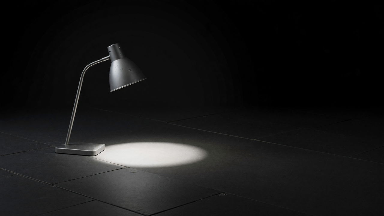 A desk lamp bent over an empty circle of light on a dark tiled floor.