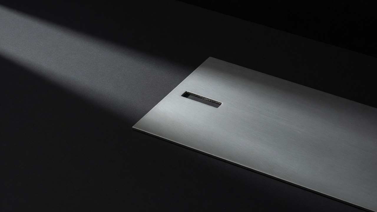 A flat brushed-steel plate with one precisely machined slot, lit from one side.