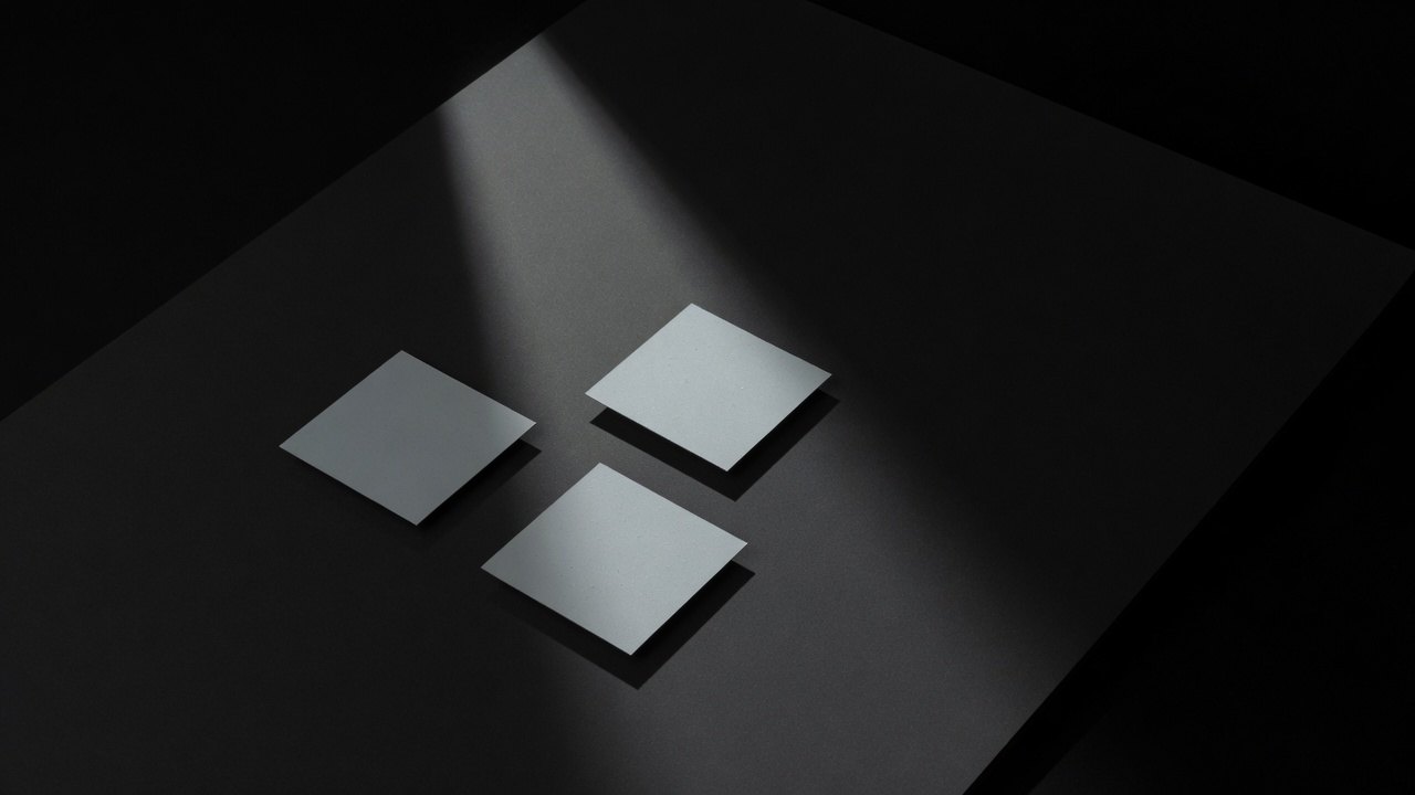 Two separate identical pale cards lying apart on a dark surface, square to the frame.